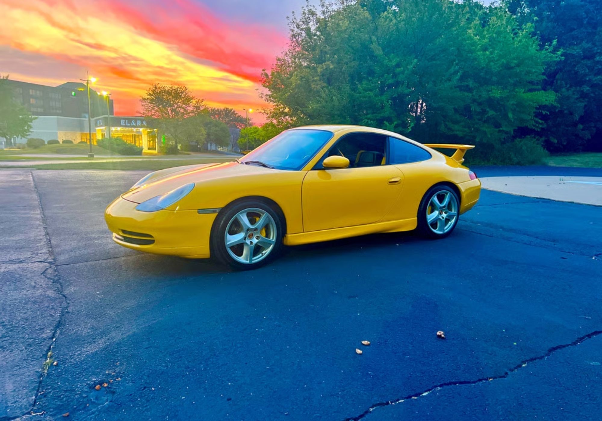 A yellow Porsche 911 in a parking lot at sunset