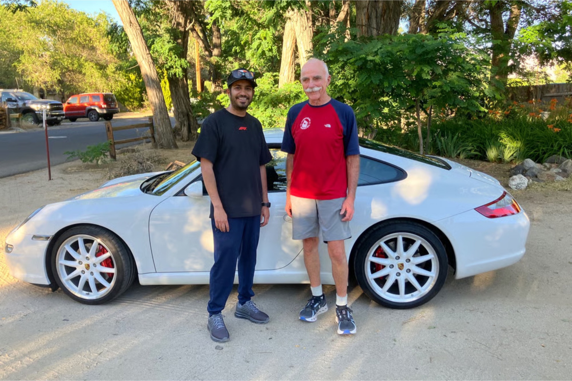 Two men standing beside a white Porsche 911