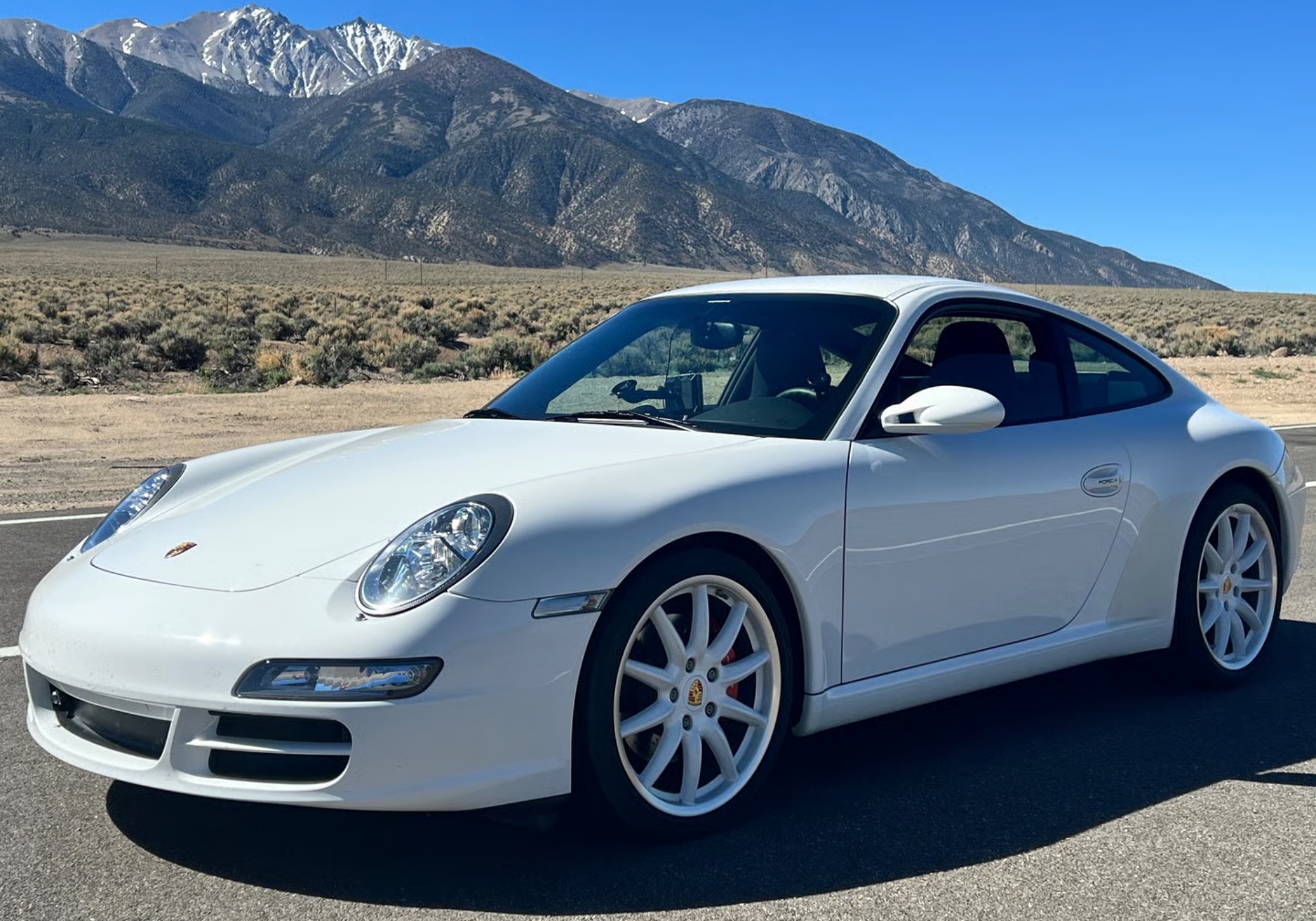 A white Porsche 911 on a desert road below snow-capped mountains
