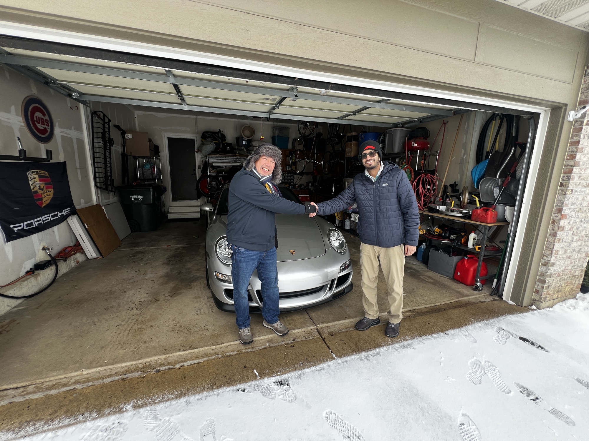 A handshake over a silver Porsche 911 in a snowy home garage