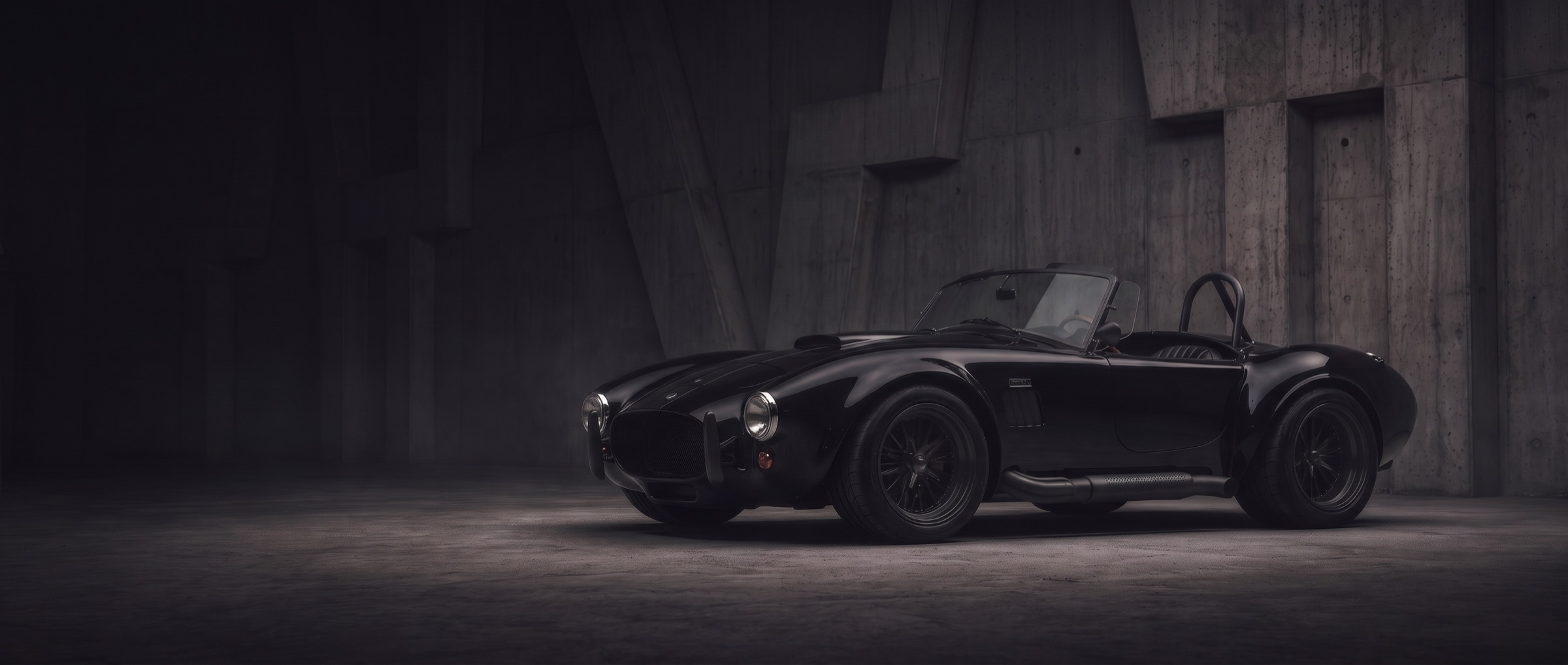 A black Cobra roadster with blacked-out pipes and roll bar in a concrete hall