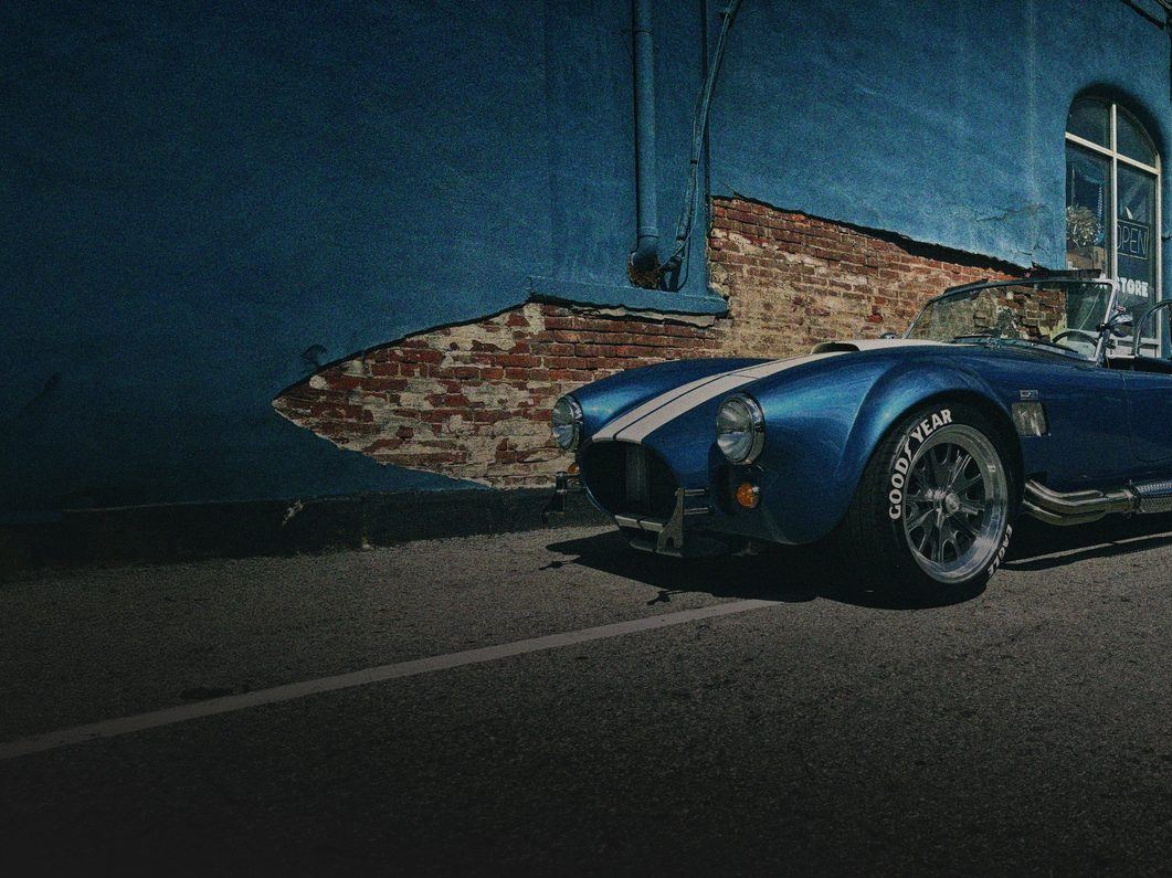 Blue Cobra roadster with white stripes, parked at night